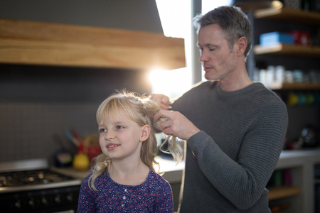 Father styling daughters hair while standing in the kitchenの写真素材