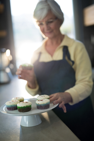 Close-up of senior woman picking up the cupcake from the trayの写真素材
