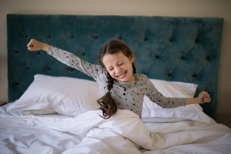 Girl stretching her arms while waking up in bedroom at homeの写真素材