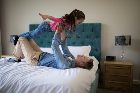 Happy father and daughter having fun on bed in bedroom at homeの写真素材