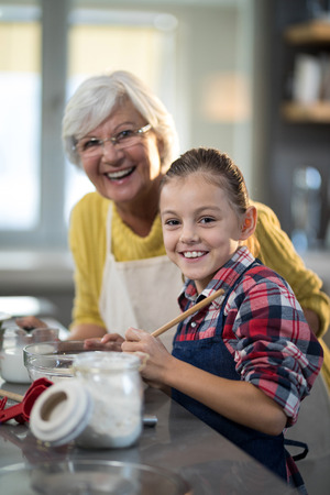 Smiling granddaughter and grandmother posing while standing in the kitchen