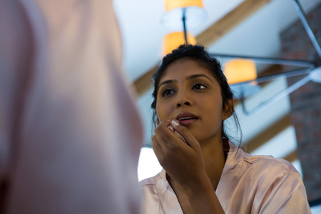 Young woman applying lip gloss reflecting on mirror at homeの写真素材