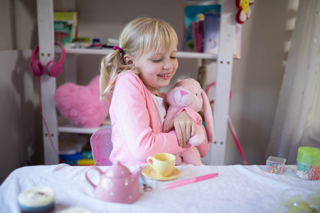 Close-up of smiling girl playing with a teddy bear and toy kitchen setの写真素材