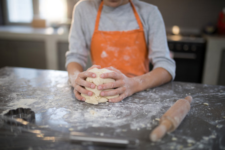 Mid section of little girl holding dough in her hand on the kitchen counterの写真素材