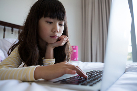 Girl using laptop while lying down on bed at homeの写真素材