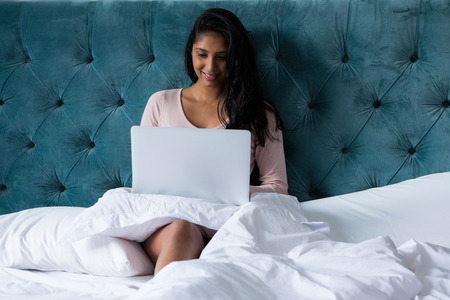Young woman using laptop on bed at homeの写真素材