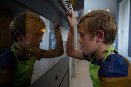 Side view of boy looking into oven in kitchen at homeの写真素材