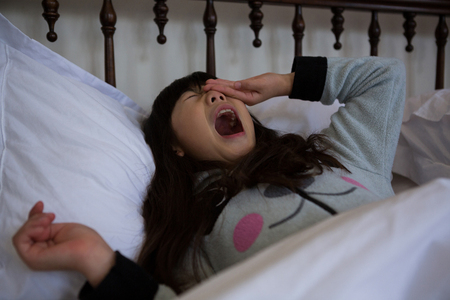 Lazy girl yawning on bed at homeの写真素材