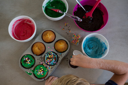 Cropped hand of boy decorating cupcakes with sprinklers at kitchen counterの写真素材