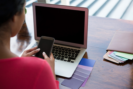 Woman with laptop using phone by table at homeの写真素材