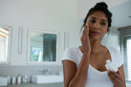 Young woman applying lotion in bathroom at homeの写真素材
