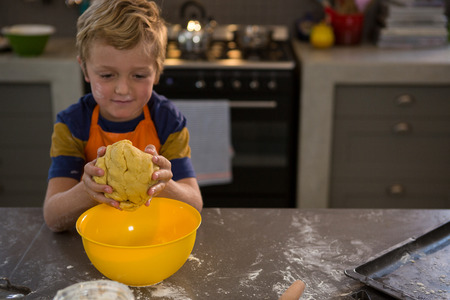 Boy kneading dough over yellow bowl at kitchen counterの写真素材