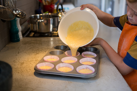 Boy pouring batter in cupcake holders at kitchen counterの写真素材