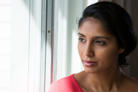Young woman looking through window at home