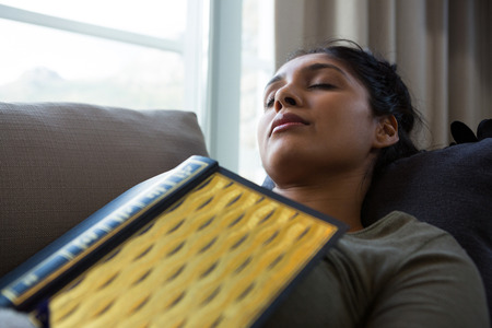 Young woman with book sleeping on sofa at home
