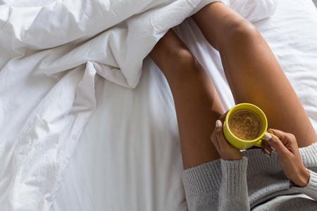 Midsection of woman holding coffee mug while relaxing on bedの写真素材