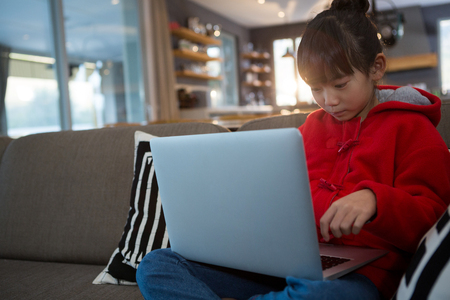 Relaxed girl using laptop on sofa in living room at homeの写真素材