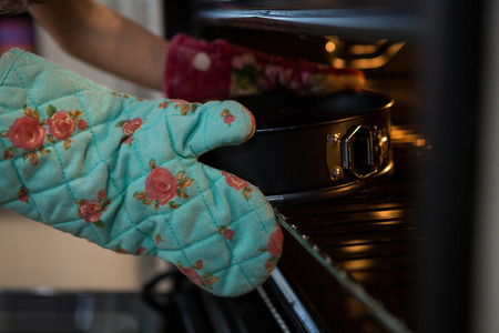 Cropped hands of girl wearing glove keeping container with cake in oven at kitchenの写真素材