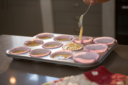 Cropped hand pouring batter in cupcake holder on counter at kitchenの写真素材