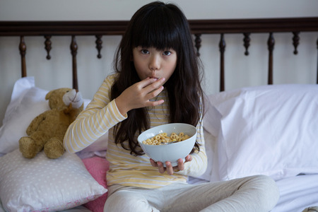 Portrait of girl eating breakfast on bed at homeの写真素材