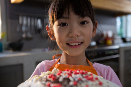 Close-up portrait of girl with cake in kitchen at homeの写真素材