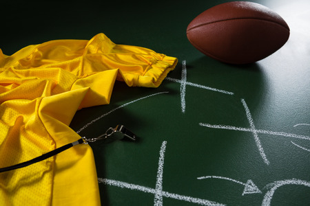 Close-up of American football jersey, whistle and football lying on green board with strategy drawn on itの写真素材