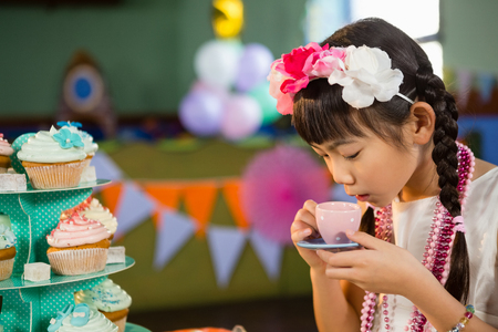 Cute girl drinking tea during birthday party at homeの写真素材
