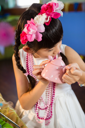 Close-up of cute girl holding toy teapot during birthday party at homeの写真素材