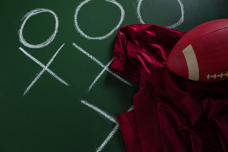 Close-up of American football jersey and football lying on green board with strategy drawn on it
