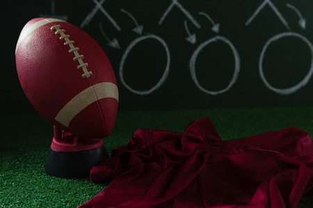 Close-up of American football jersey and football lying on artificial turf against strategy boardの写真素材