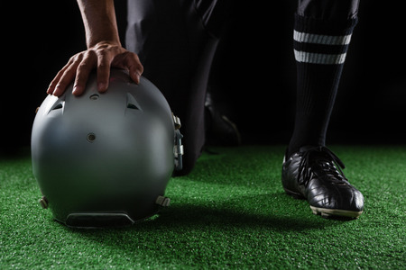 Close-up of American football player resting his hands on head gear kept on artificial grassの写真素材