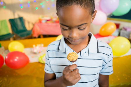 Cute boy holding lollipop during birthday party at homeの写真素材