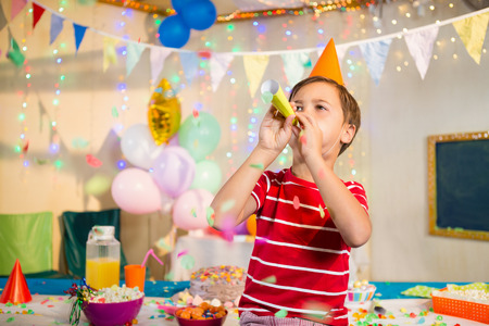 Cute boy blowing party horn during birthday party at homeの写真素材