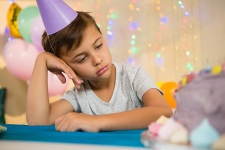 Thoughtful boy sitting near a birthday cake at homeの写真素材
