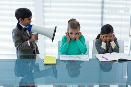 Businesswomen closing ears while businessman screaming in megaphone at officeの写真素材