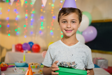 Portrait of boy holding a gift box during birthday party at home
