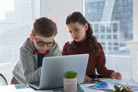 Business people discussing over laptop while standing at table in officeの写真素材