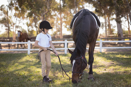 Full length of girl wearing helmet standing by horse on field in paddockの写真素材