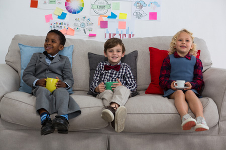 Portrait of business people having drink while relaxing on sofa in creative officeの写真素材