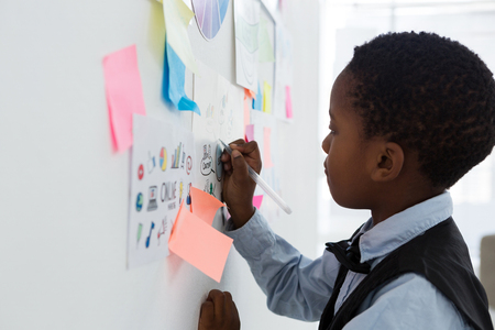 Side view of businessman writing on paper at whiteboard in creative officeの写真素材