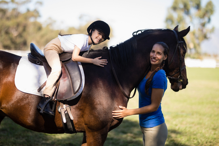 Portrait of smiling jockey and girl embracing horse at paddockの写真素材