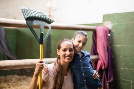 Portrait of female jockey holding rake with sister in stableの写真素材
