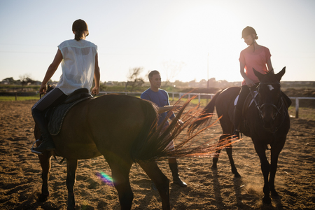 Trainer guiding female friends in riding horse at barnの写真素材