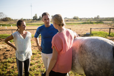 Trainer guiding women while standing by horse at barnの写真素材
