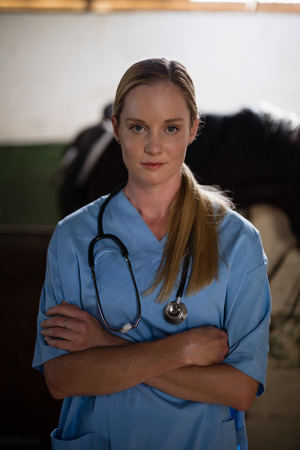 Portrait of female vet with arms crossed with horse standing in backgroundの写真素材