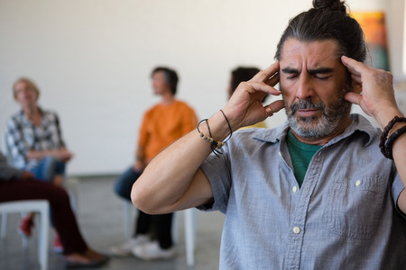 Man with head in hand sitting on chair while friends discussing in background at art class