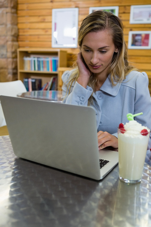 Young woman using laptop while sitting at cafeの写真素材