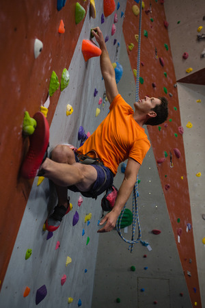 Low angle view of confident man wall climbing in gymの写真素材