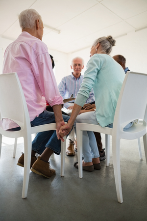 Low angle view of senior friends holding hands while sitting on hair in art classの写真素材