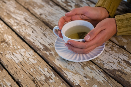 Cropped hand of woman holding tea at wooden tableの写真素材